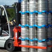 Forklift handling stacked stainless steel kegs secured with blue plastic spacers outdoors.