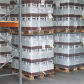 Warehouse shelves stacked with multiple pallets of white plastic storage containers wrapped in plastic film.
