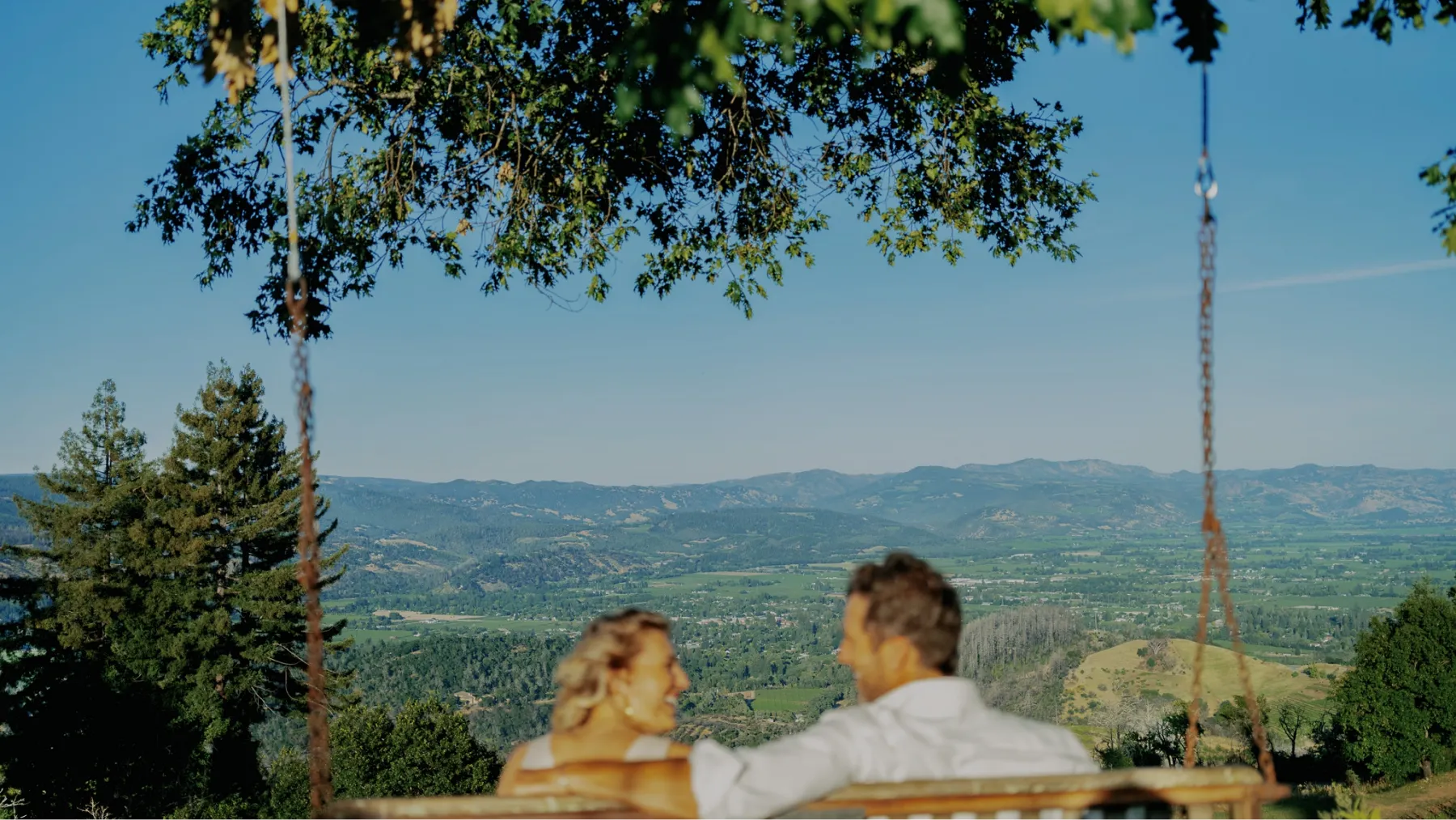 A man and woman enjoying glasses of wine on an elegant porch with outdoor seating, surrounded by lush greenery.