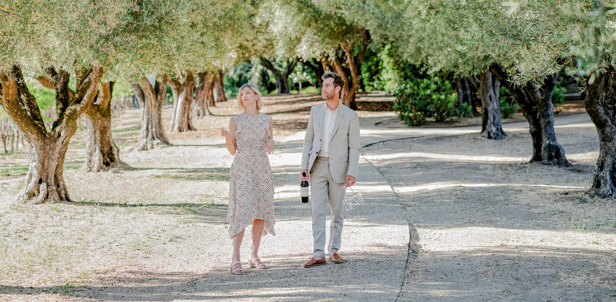 A man and woman enjoying glasses of wine on an elegant porch with outdoor seating, surrounded by lush greenery.