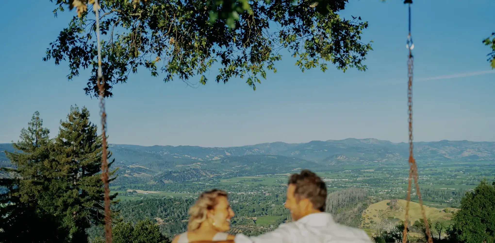 A man and woman enjoying glasses of wine on an elegant porch with outdoor seating, surrounded by lush greenery.