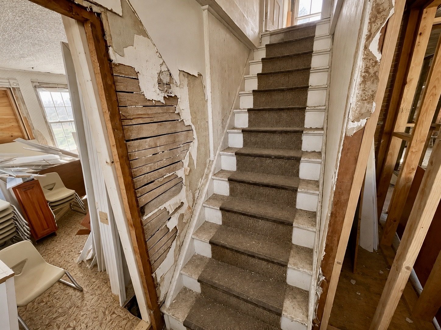 The original staircase with worn carpet treads and horsehair plaster pulled off the wall to bare lath