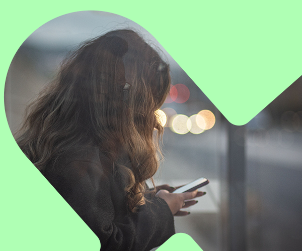 Kvinna som tittar på sin telefon vid en busshållplats med ett grönt grafiskt element ovanpå.