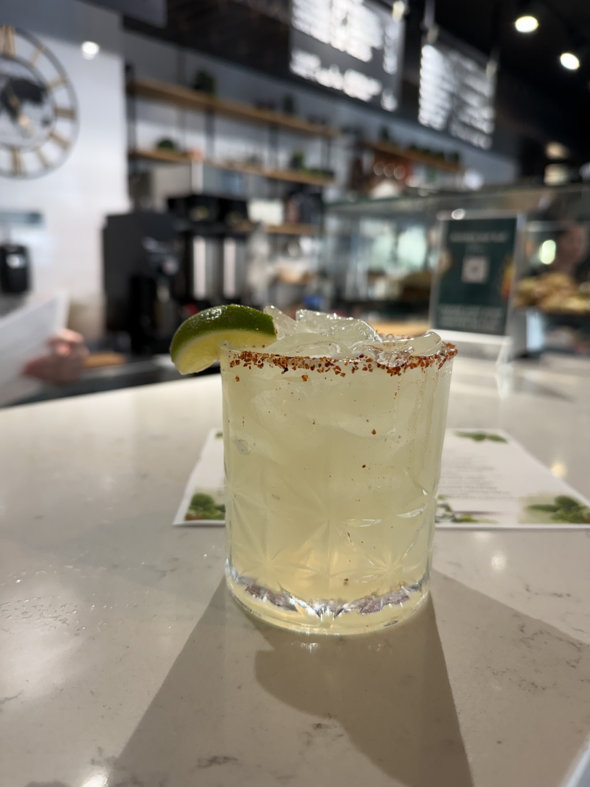 Last Train Home cocktail with a chili-salt rim and lime wedge on the cafe counter, espresso machine behind