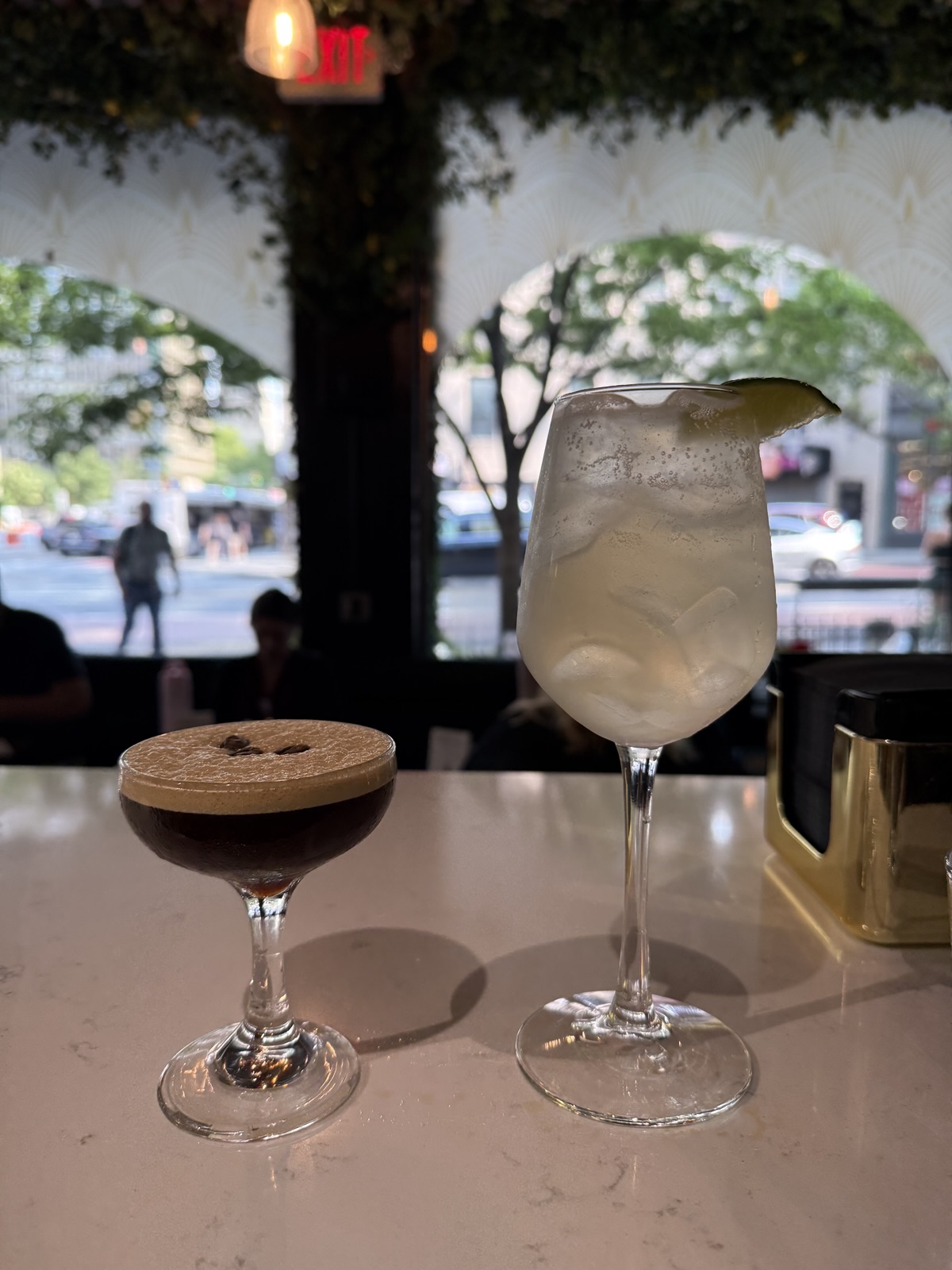 The Station Espresso Martini and a Platform 34 cocktail side by side on the marble bar, with 2nd Avenue visible through the arched window behind