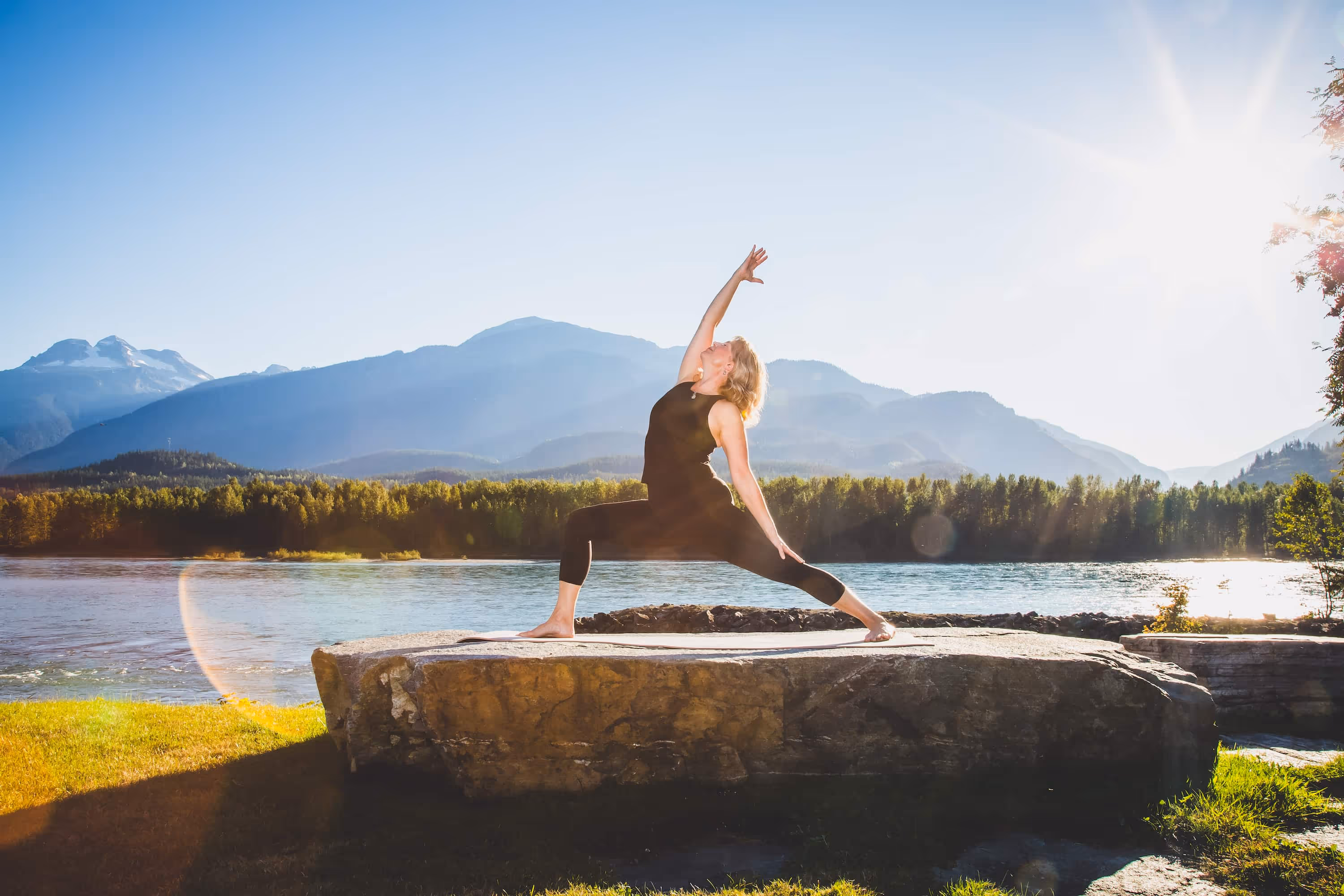 Sheri doing reverse warrior yoga pose with sunset, river and mountains behind her. 