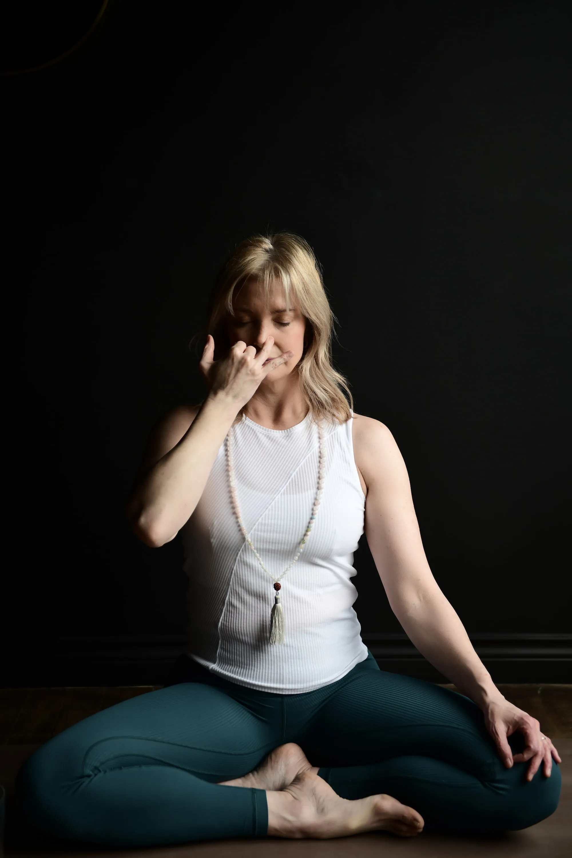 Sheri sitting on floor, legs crossed, with hand touching nose.