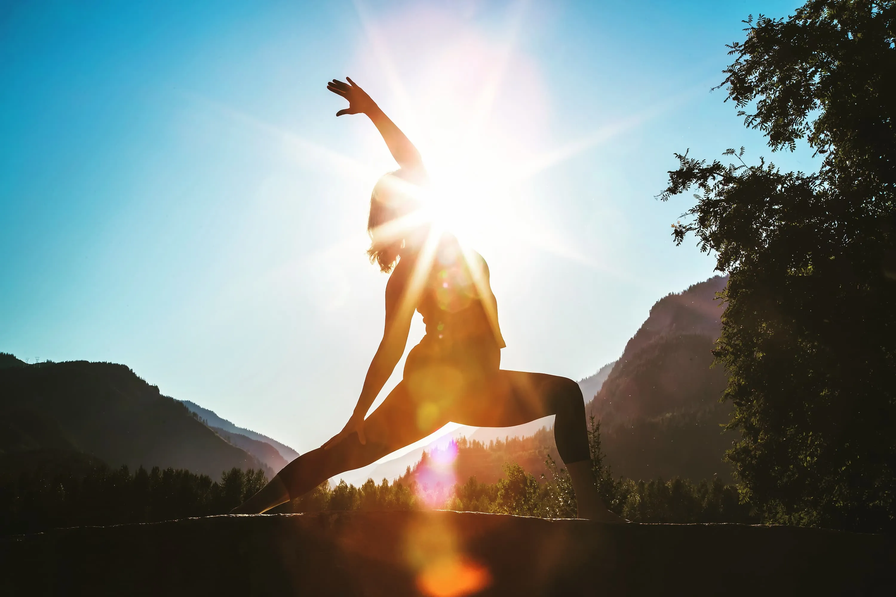Sheri doing reverse warrior yoga pose outside with sun flares behind her.