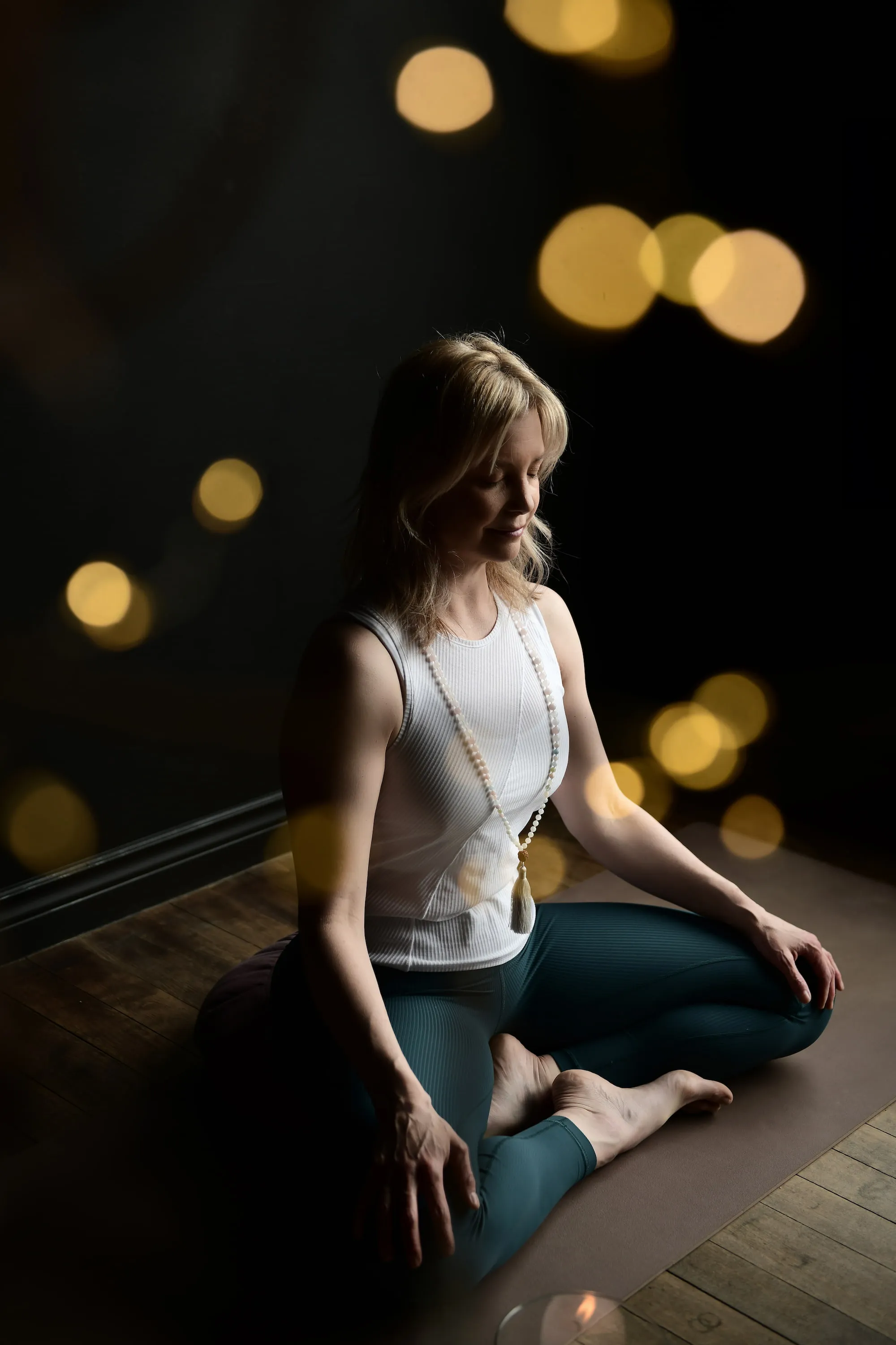 Sheri weather white top, green pants sitting cross legged on the floor.