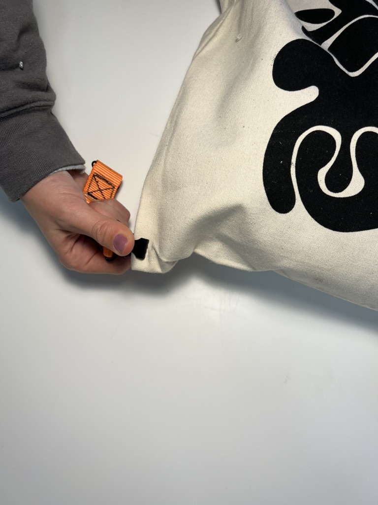 ©Tim Engel Auf dem Foto ist eine Hnad zu sehen, die einen Clip an einer Jutetasche befestigt.