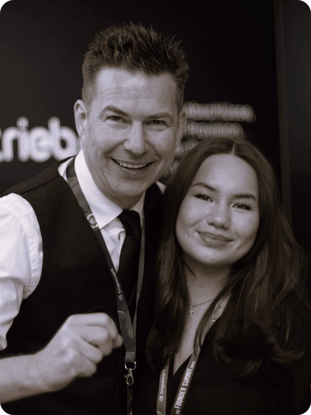 Mann und Frau lächeln in die Kamera, beide tragen Namensschilder, Hintergrund dunkel.