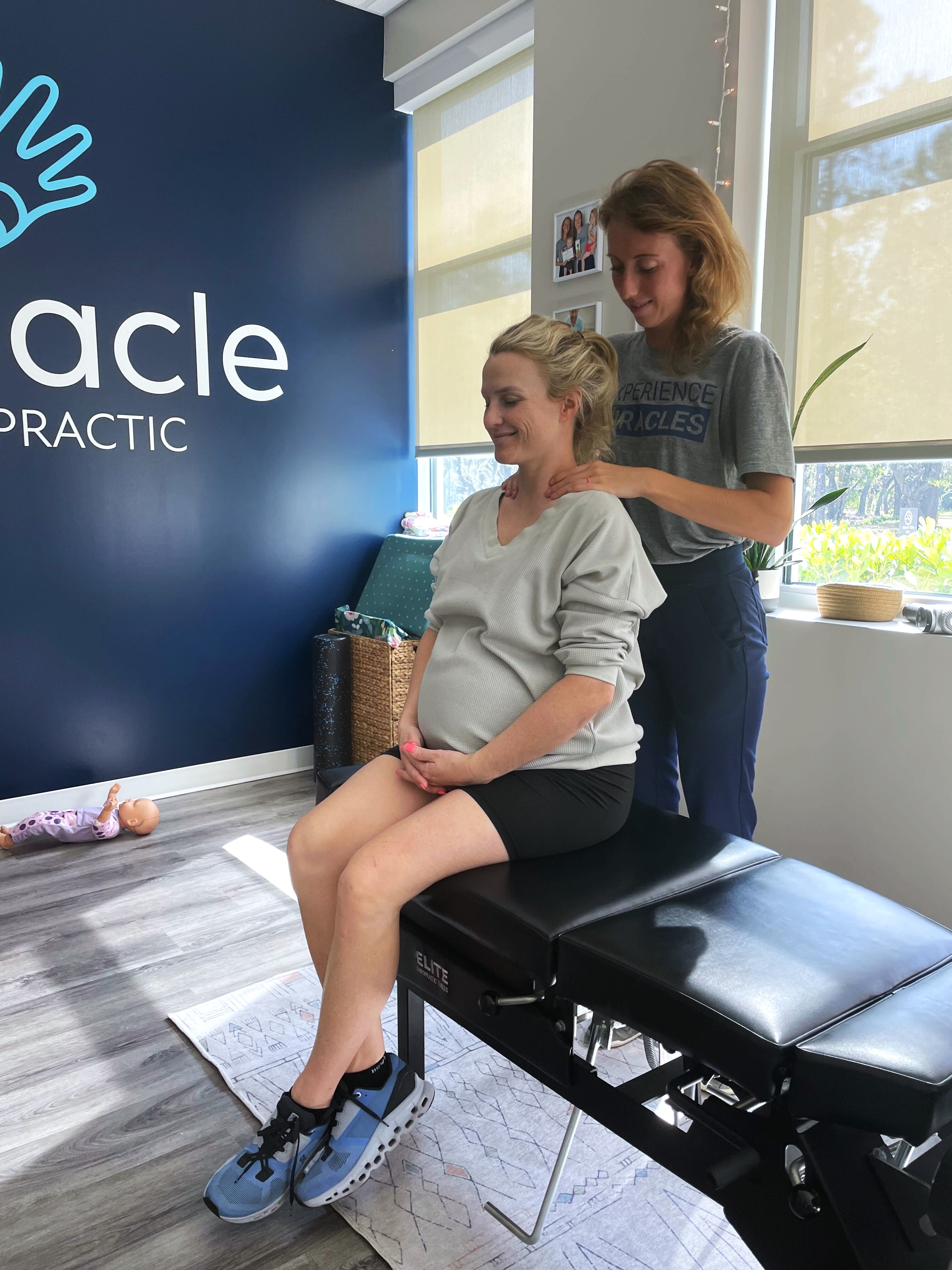 Pregnant woman receiving prenatal chiropractic care from a female chiropractor in a calm, modern clinic for pregnancy well...