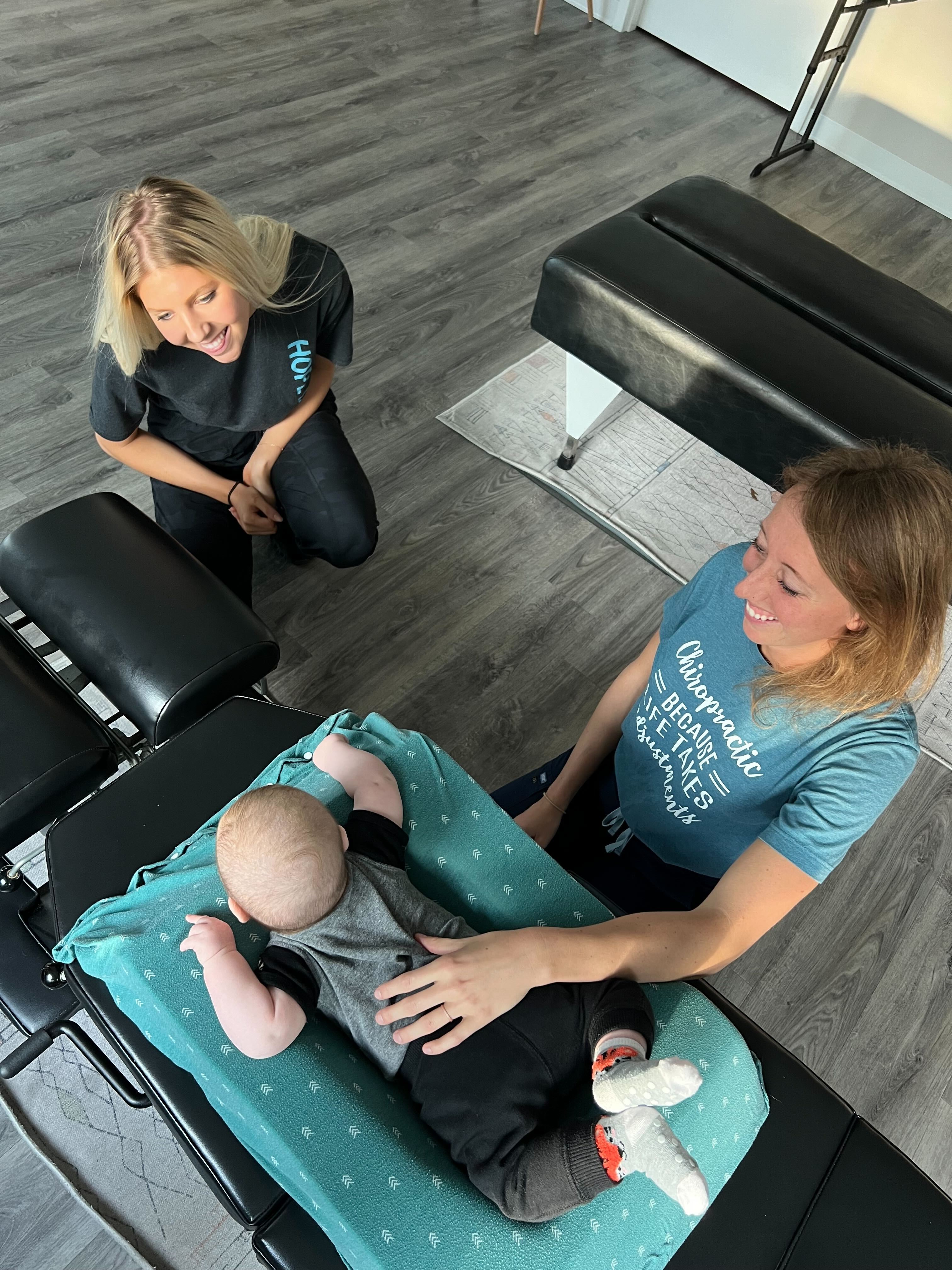 Young mother and chiropractor providing gentle infant chiropractic care in a modern family wellness clinic setting.