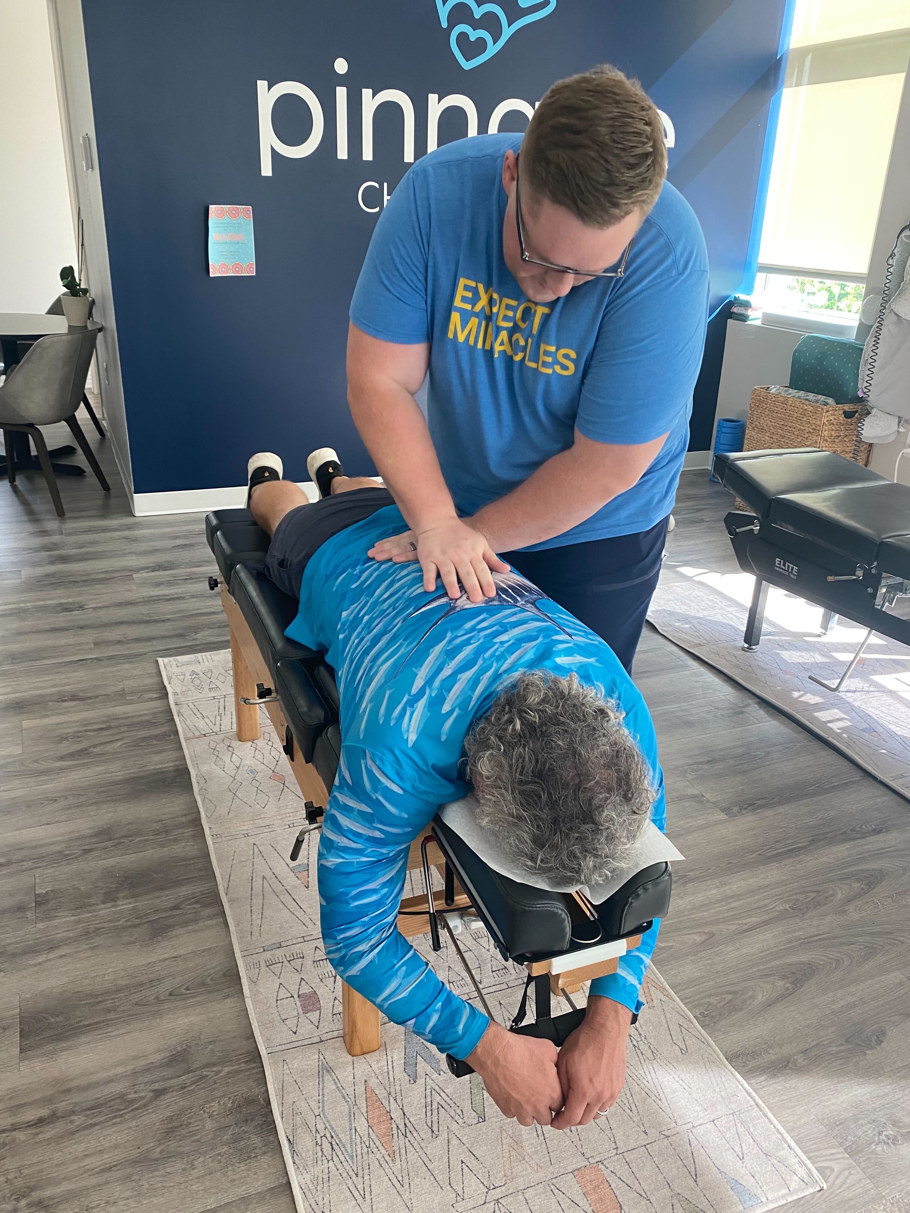 Young chiropractor performing spinal adjustment on middle-aged patient in modern clinic for back pain relief and wellness.