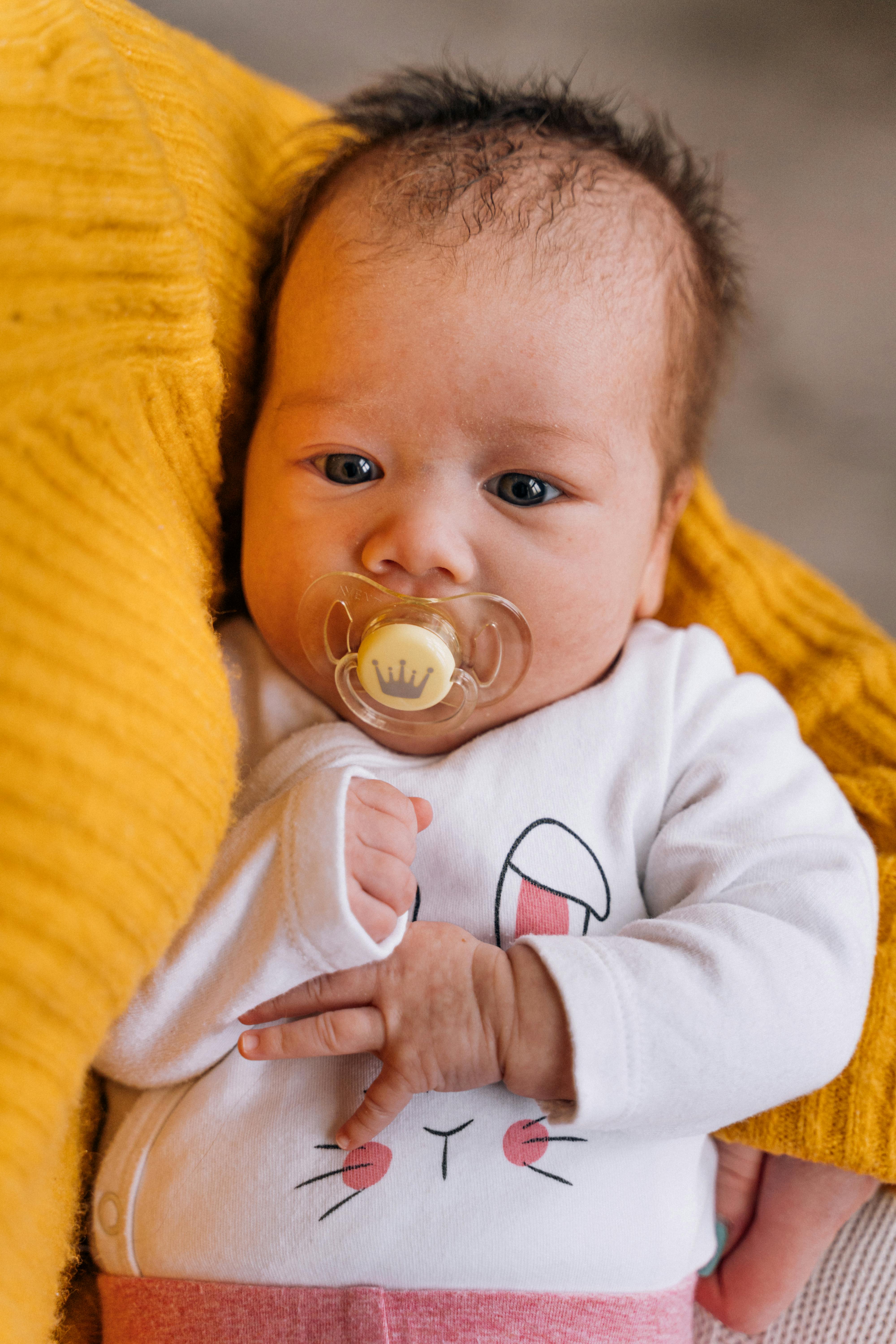 Baby with hiccups lying on their back smiling, supported by mom’s hands