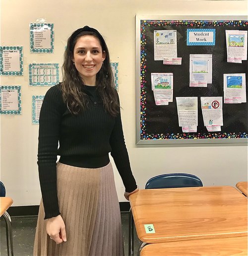Rebecca Yonk smiling in her classroom near student work display