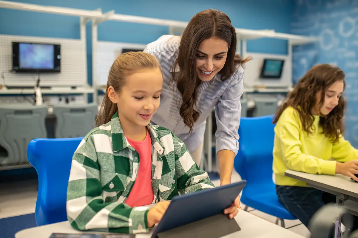 image with a teacher with her student using tech devices in class