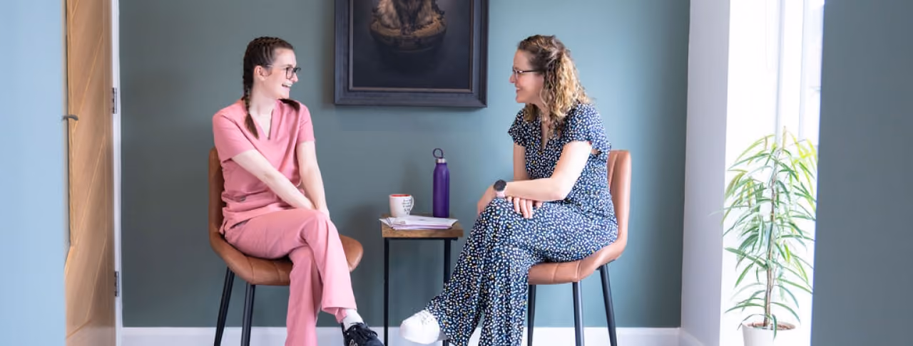 two women sitting on chairs talking in a room