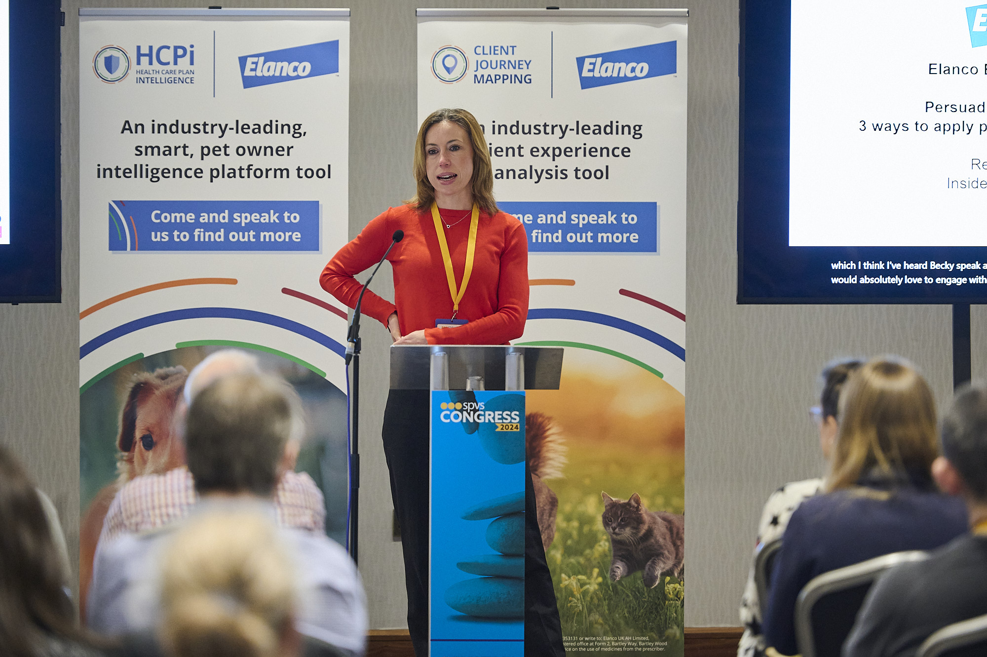 Woman in orange sweater speaking at a podium during a pet industry conference.