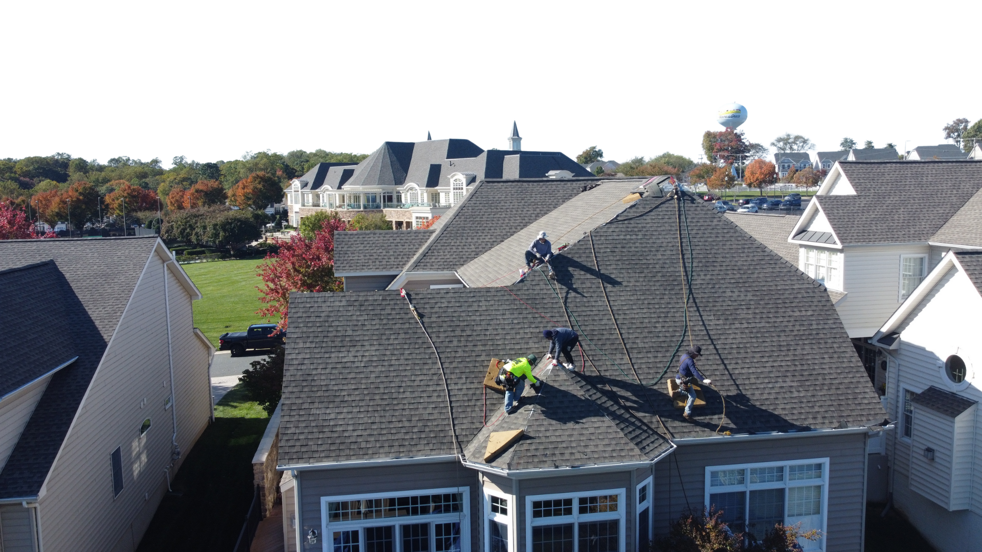 Four workers installing or repairing a shingled roof on a residential house on a clear sunny day.