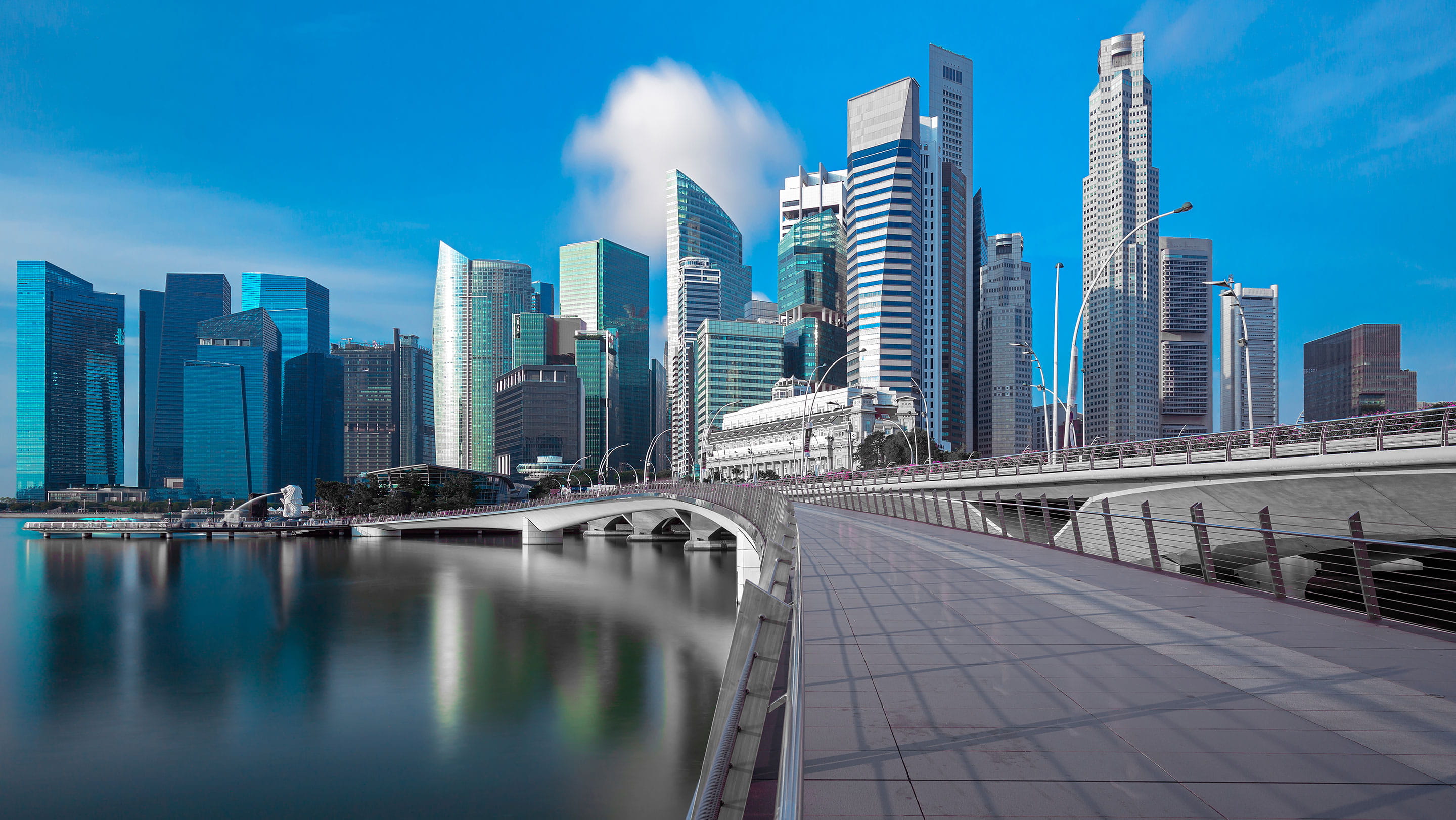Singapore's financial district skyline at Marina Bay, featuring modern skyscrapers, the Esplanade Bridge and waterfront architecture reflected in the water.
