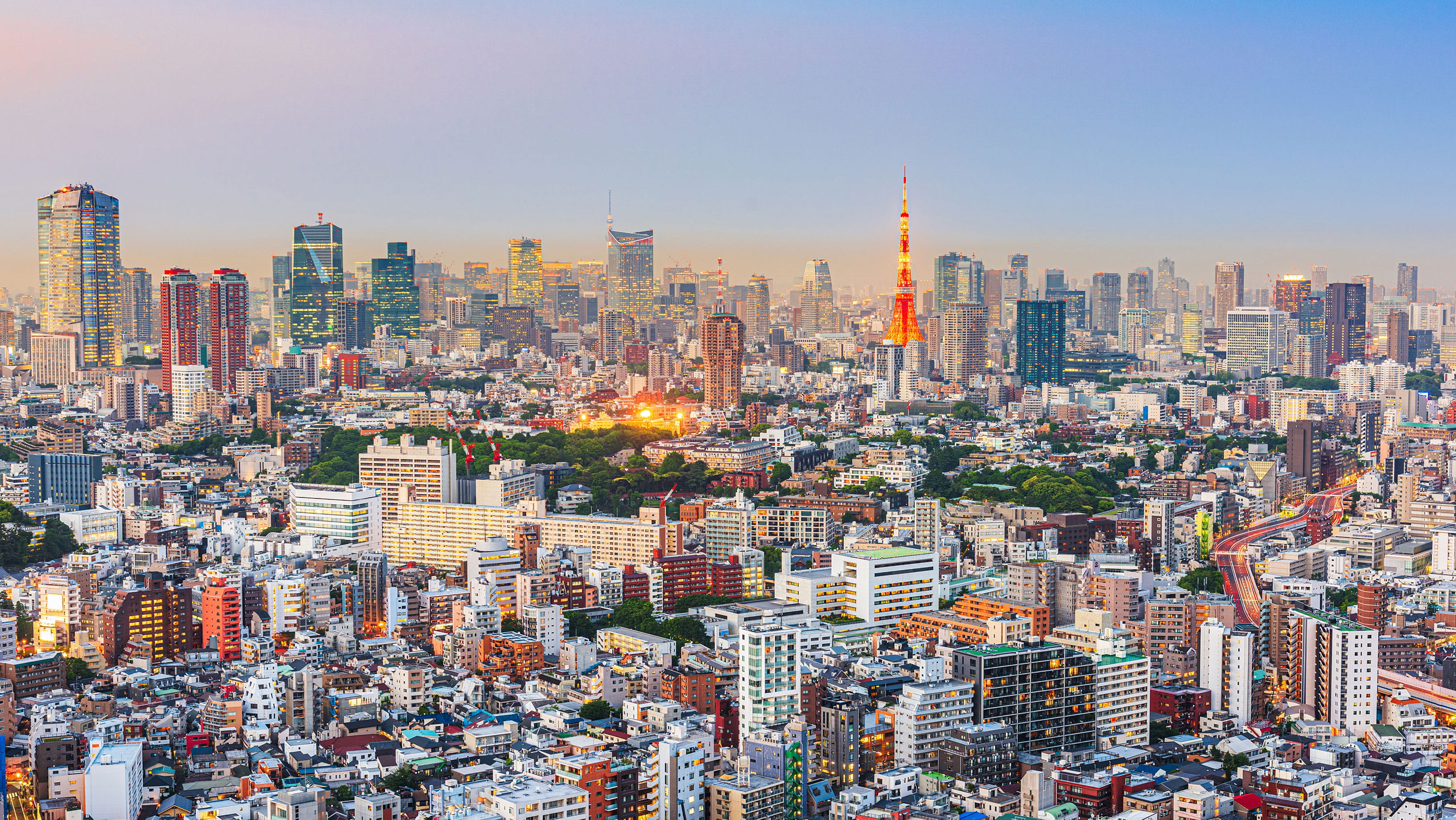 Panoramic view of Tokyo's skyline at dusk, featuring the illuminated Tokyo Tower surrounded by modern skyscrapers and residential buildings.