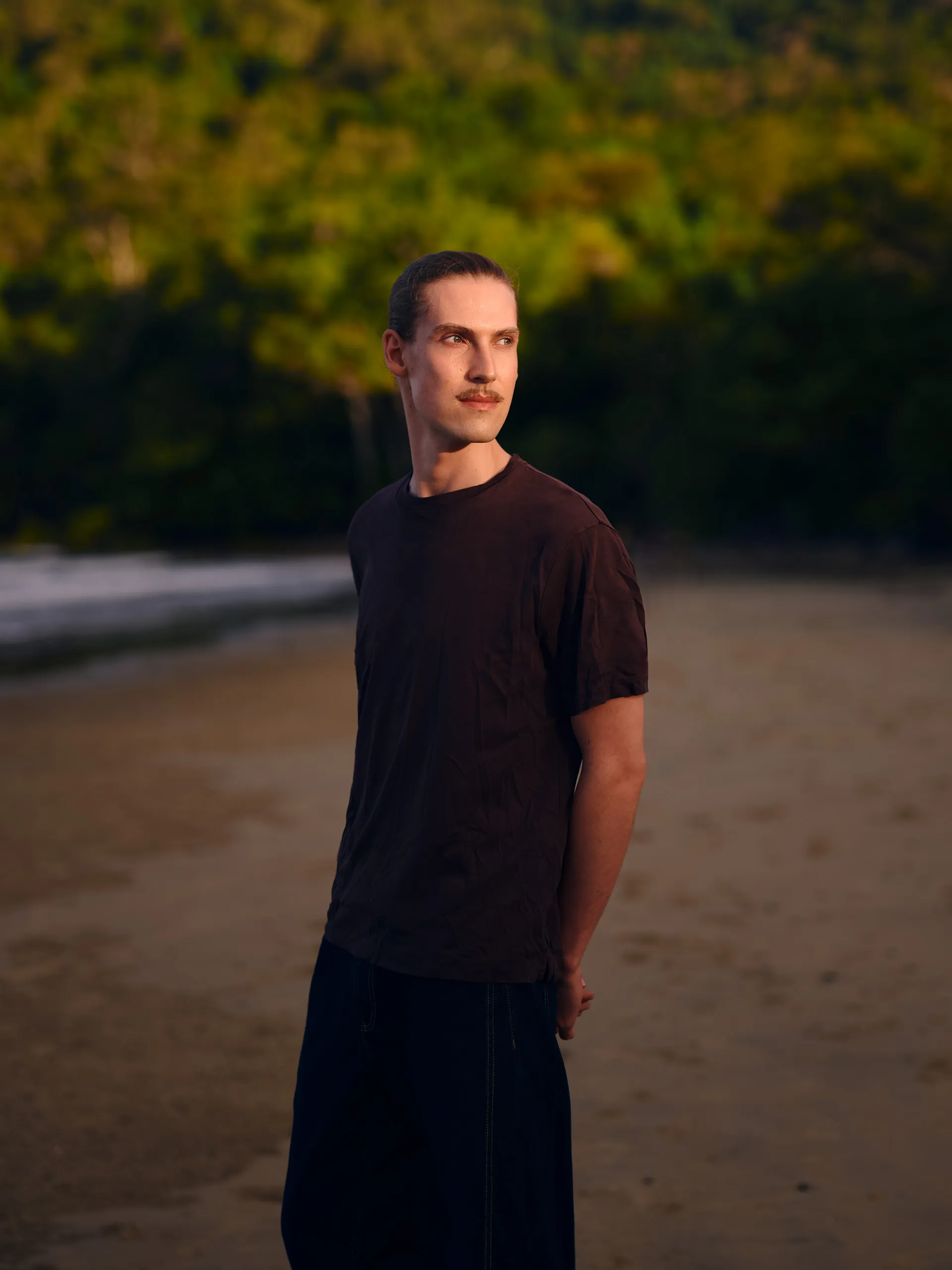 Portrait von Fotograf Juri Seger vor einem Regenwald. Blick zur Linken seite vom Bild mit einem leichten Lächeln und Armen hinter dem Rücken
