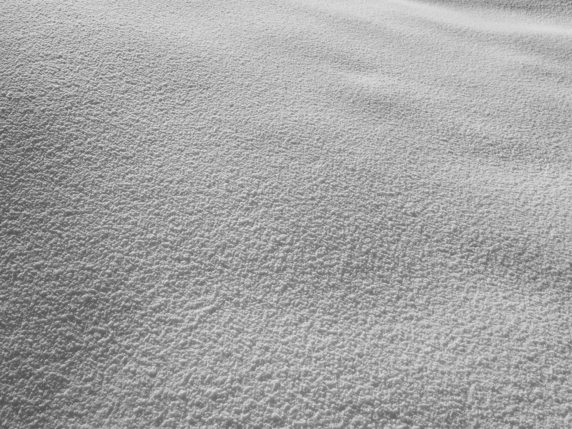 Nahaufnahme von feinem Schnee mit einer leicht unebenen Oberfläche und feiner kristalliner Struktur.