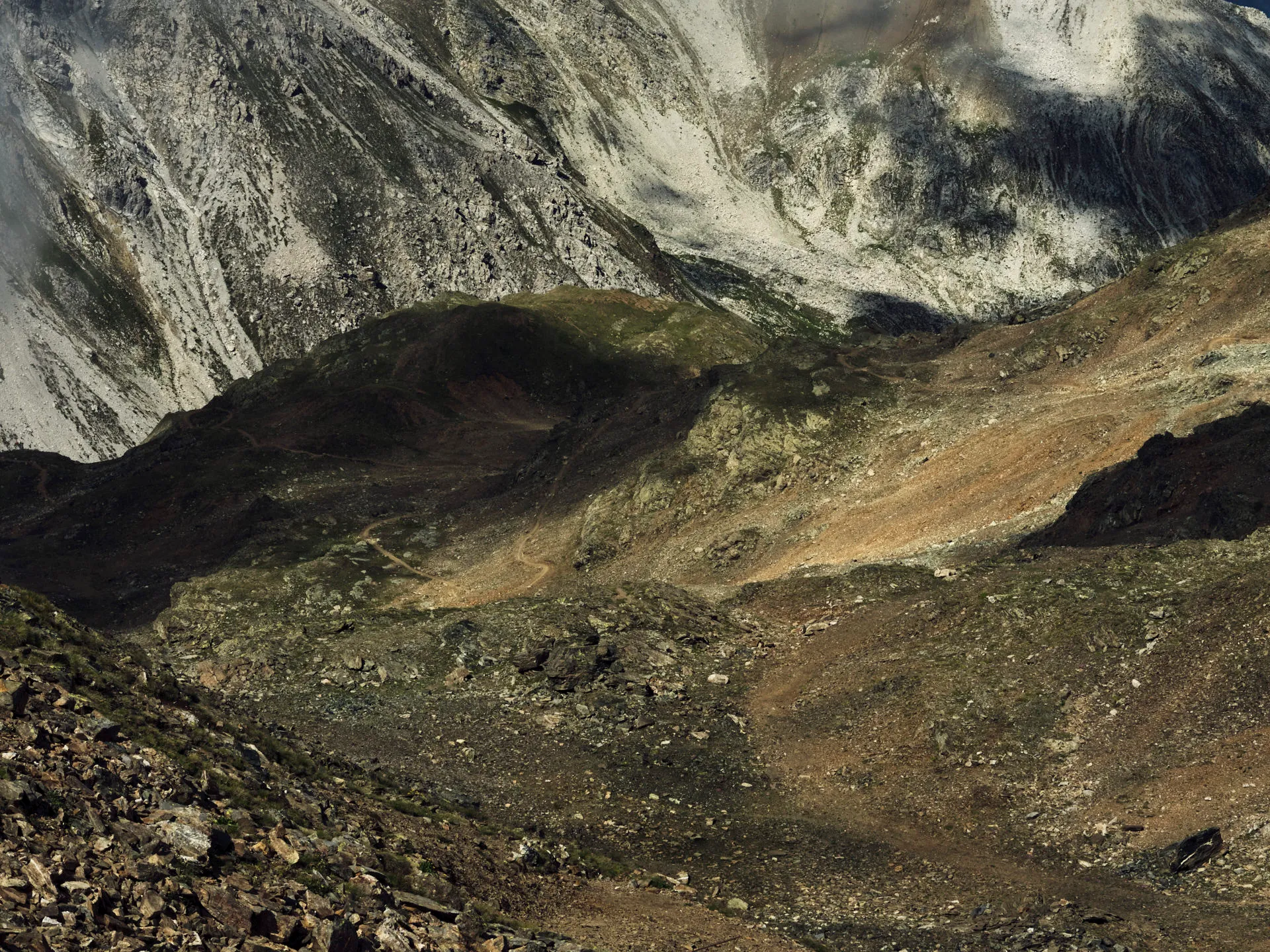 Berglandschaft mit steinigem Gelände, schmalem Wanderpfad und schattigen Bereichen, der auf höhere felsige Gipfel und Hänge führt.