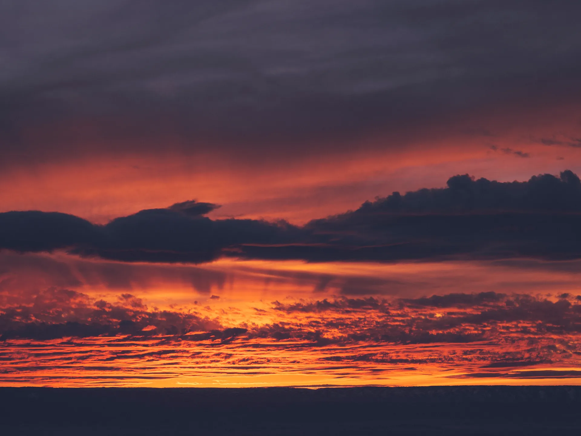 Dramatischer Sonnenuntergang mit leuchtend orangefarbenem Himmel und dunklen, sich ausbreitenden Wolken.