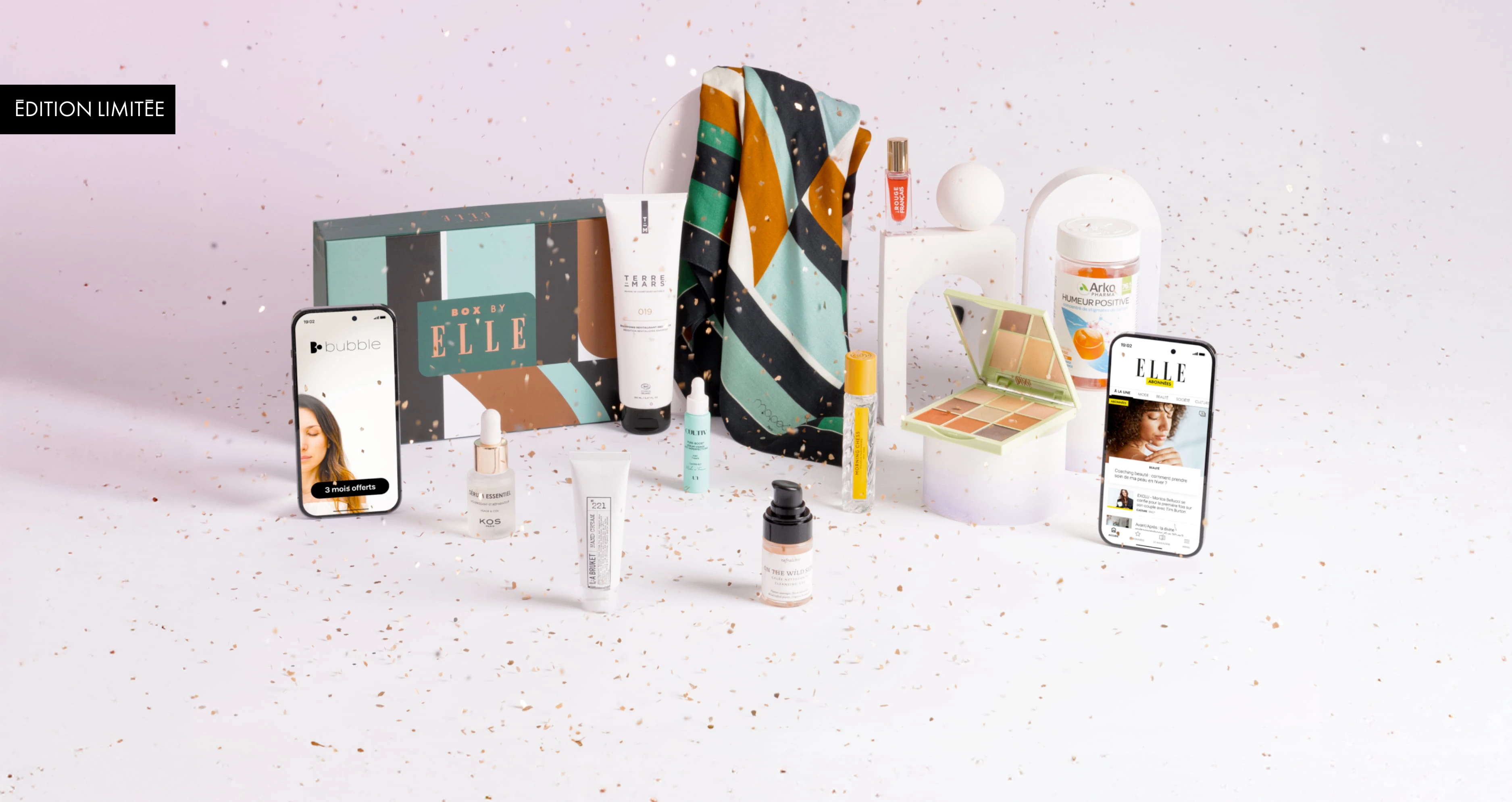Composition de la Box by ELLE en édition limitée, présentée sur fond rose clair avec des confettis dorés. La box contient divers produits bien-être et beauté : soins visage, maquillage, compléments alimentaires, foulard coloré, et deux smartphones affichant les applis ELLE et Bubble. Le coffret principal est décoré de formes géométriques vertes, brunes, noires et blanches.