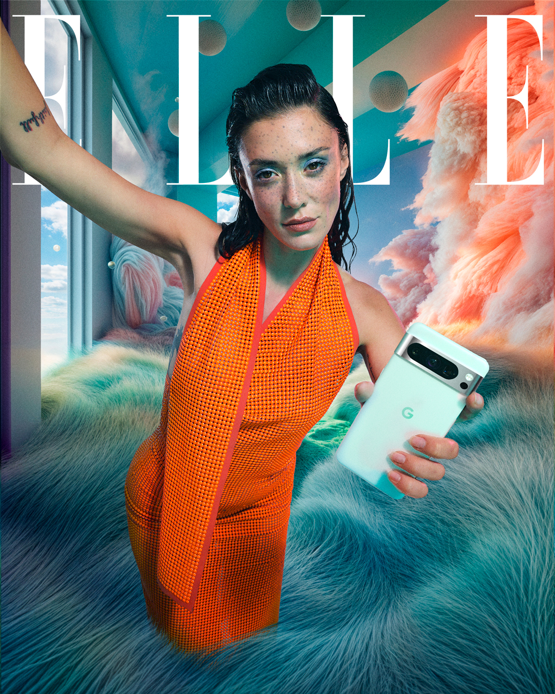 Femme aux cheveux mouillés tenant un smartphone Google Pixel blanc dans sa main droite, prenant un selfie dans un décor intérieur surréaliste. Elle porte une robe orange vif à motif grillagé. L’arrière-plan est composé de textures pelucheuses bleu-vert, de nuages roses et de formes géométriques flottantes. À gauche, une grande baie vitrée laisse apparaître un ciel bleu parsemé de lunes. Le logo "ELLE" apparaît en blanc en haut de l’image.