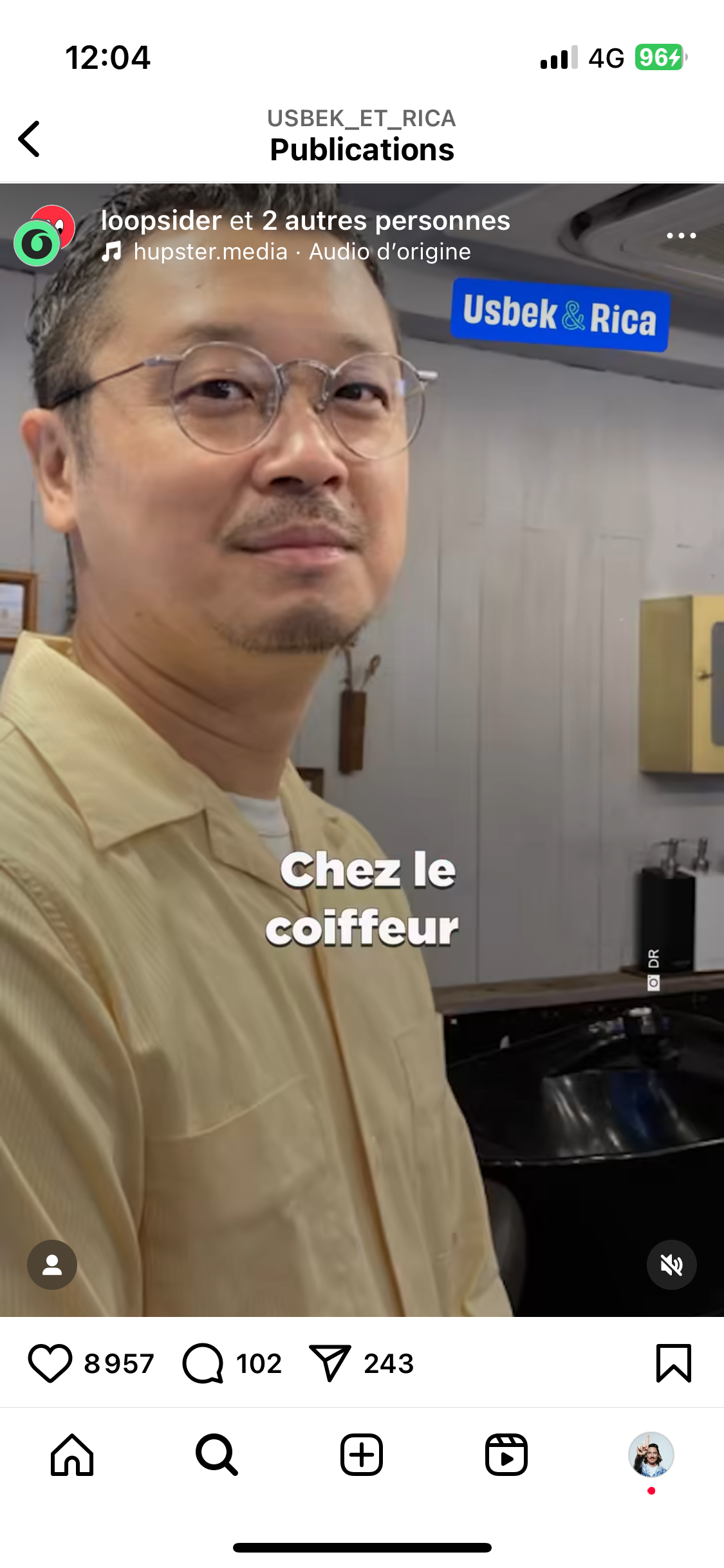 Capture d’écran d’une vidéo Instagram publiée par le compte @usbek_et_rica. Un homme asiatique portant des lunettes et une chemise beige regarde la caméra dans un salon de coiffure. Le texte “Chez le coiffeur” apparaît en blanc au centre de l’image. En haut à gauche figurent le nom de l’audio utilisé et le logo de Usbek & Rica.