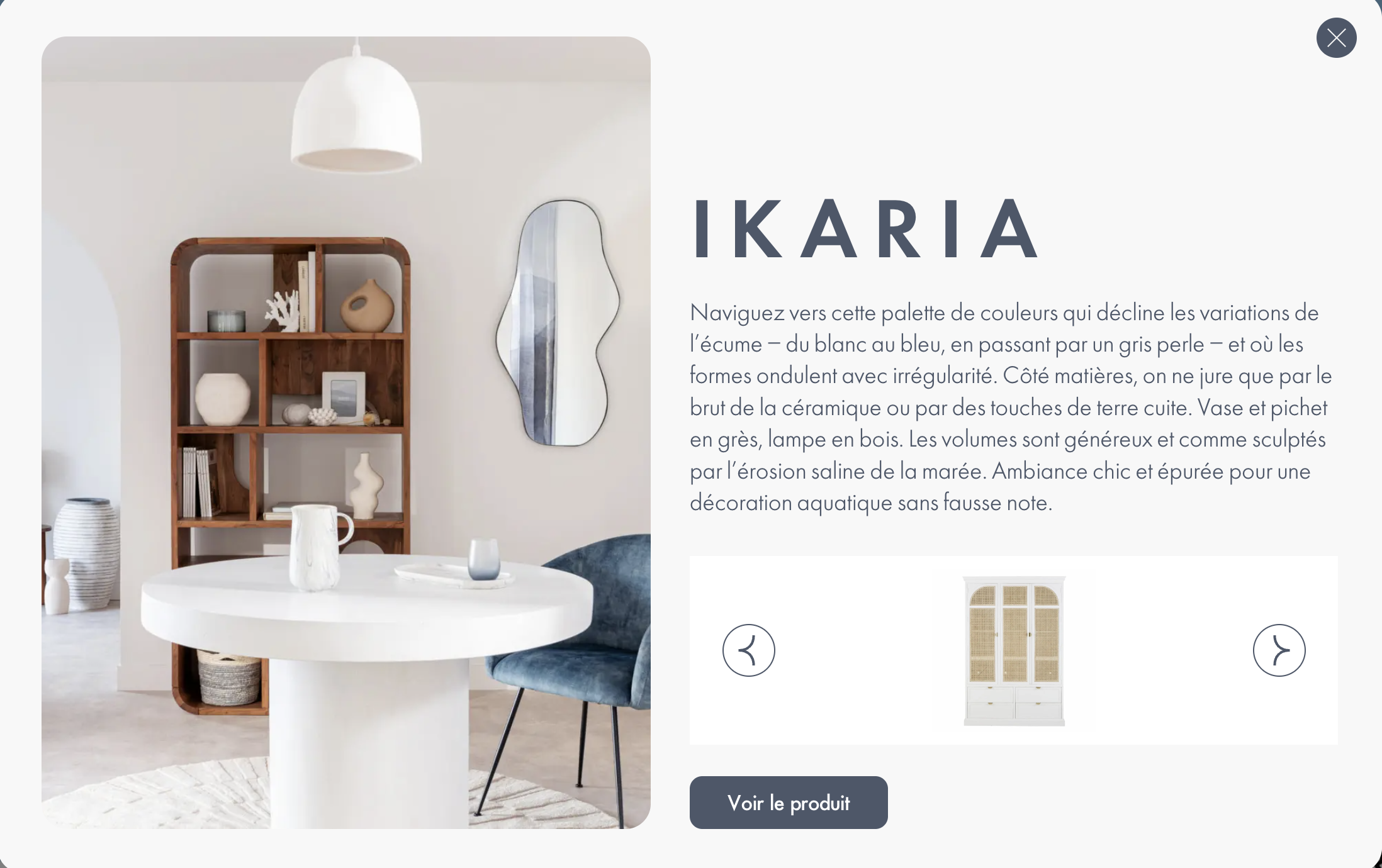 Vue d’une salle à manger épurée aux couleurs claires, composée d’une table ronde blanche, d’une chaise en velours bleu, et d’une grande étagère en bois sombre garnie d’objets en céramique. Un miroir organique et une suspension blanche complètent l’ambiance minimaliste.