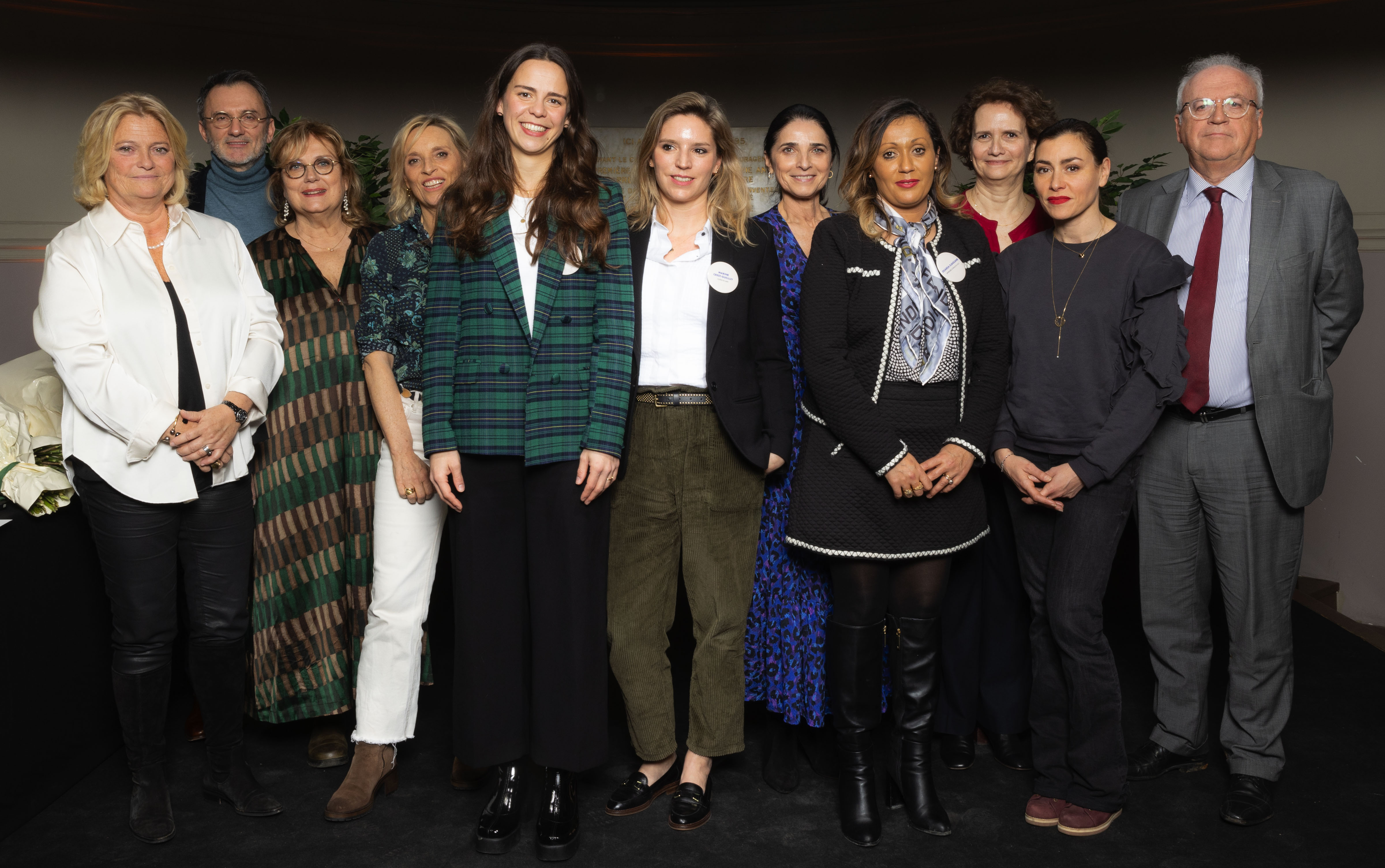 Un groupe de douze personnes, majoritairement des femmes, posent ensemble pour une photo de groupe lors d’un événement. Elles portent des tenues habillées ou professionnelles et sourient à l’objectif.