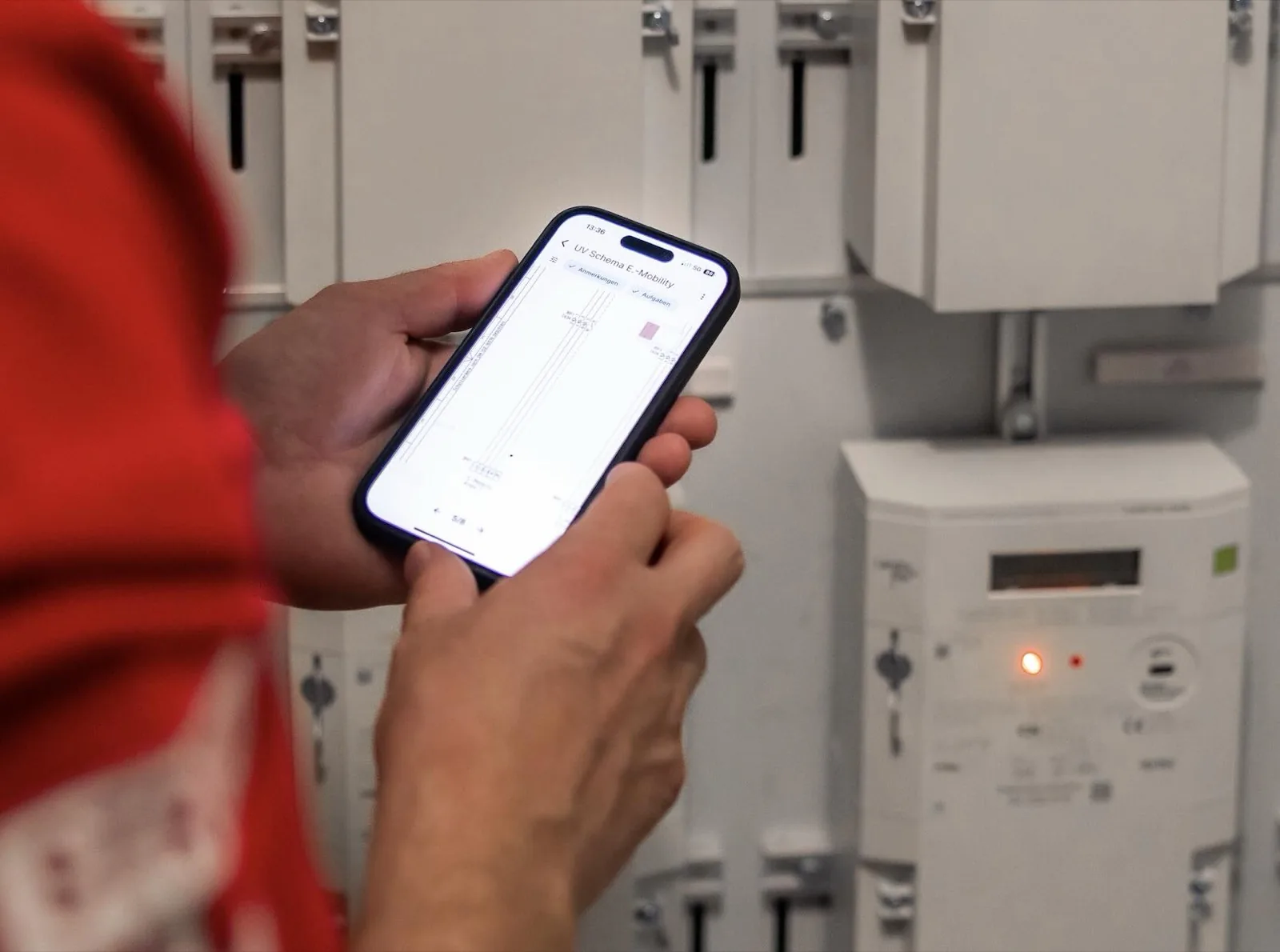 Une personne tient un smartphone avec l'application Benetics devant des armoires électriques