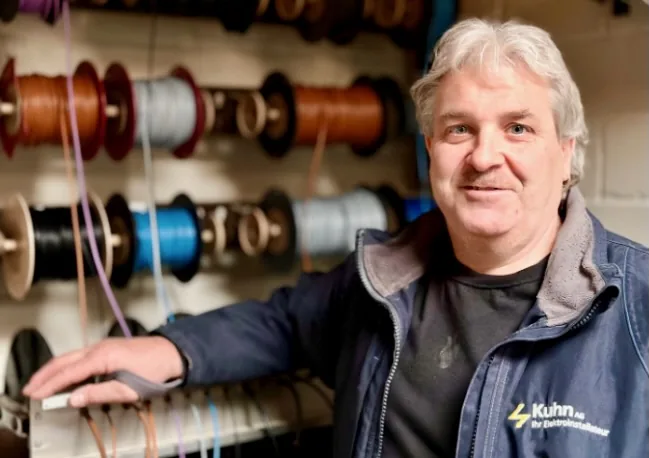 Portrait d'un employé de Kuhn AG devant des bobines de câbles dans l'atelier