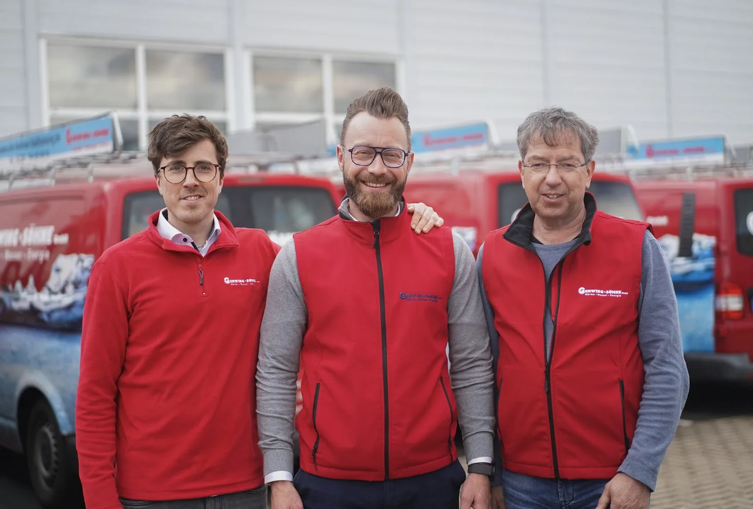 Trois collaborateurs de Gerwing & Söhne en gilets rouges de l'entreprise devant des véhicules de la société