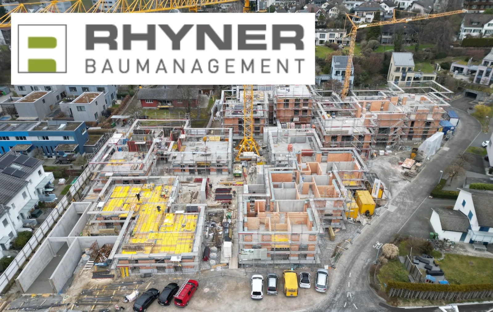 Aerial view of a Rhyner Baumanagement construction site with cranes and apartment buildings under construction