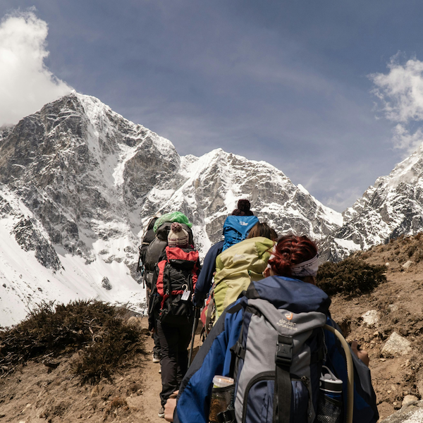 A scenic mountain range. A small group of people are hiking toward a distant snowy peak.