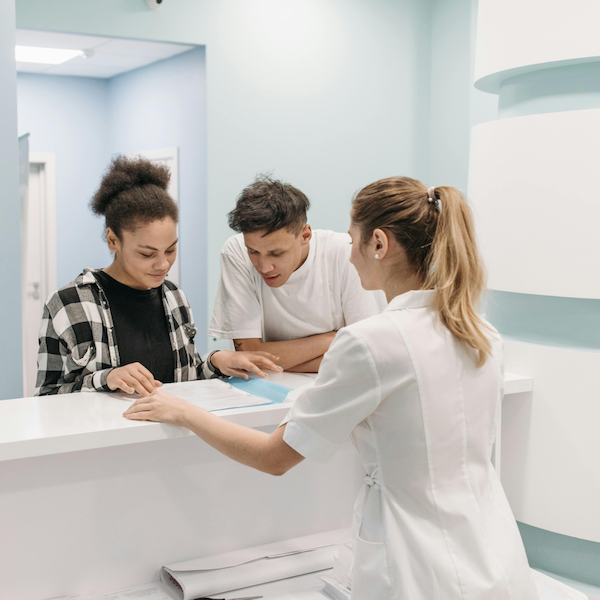 A clinical receptionist explaining how to book to two customers.