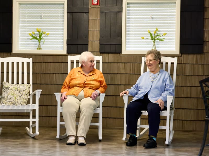 Two senior residents chatting in indoor rocking chairs at GentleBrook Assisted Living South, fostering social connection and independent living.