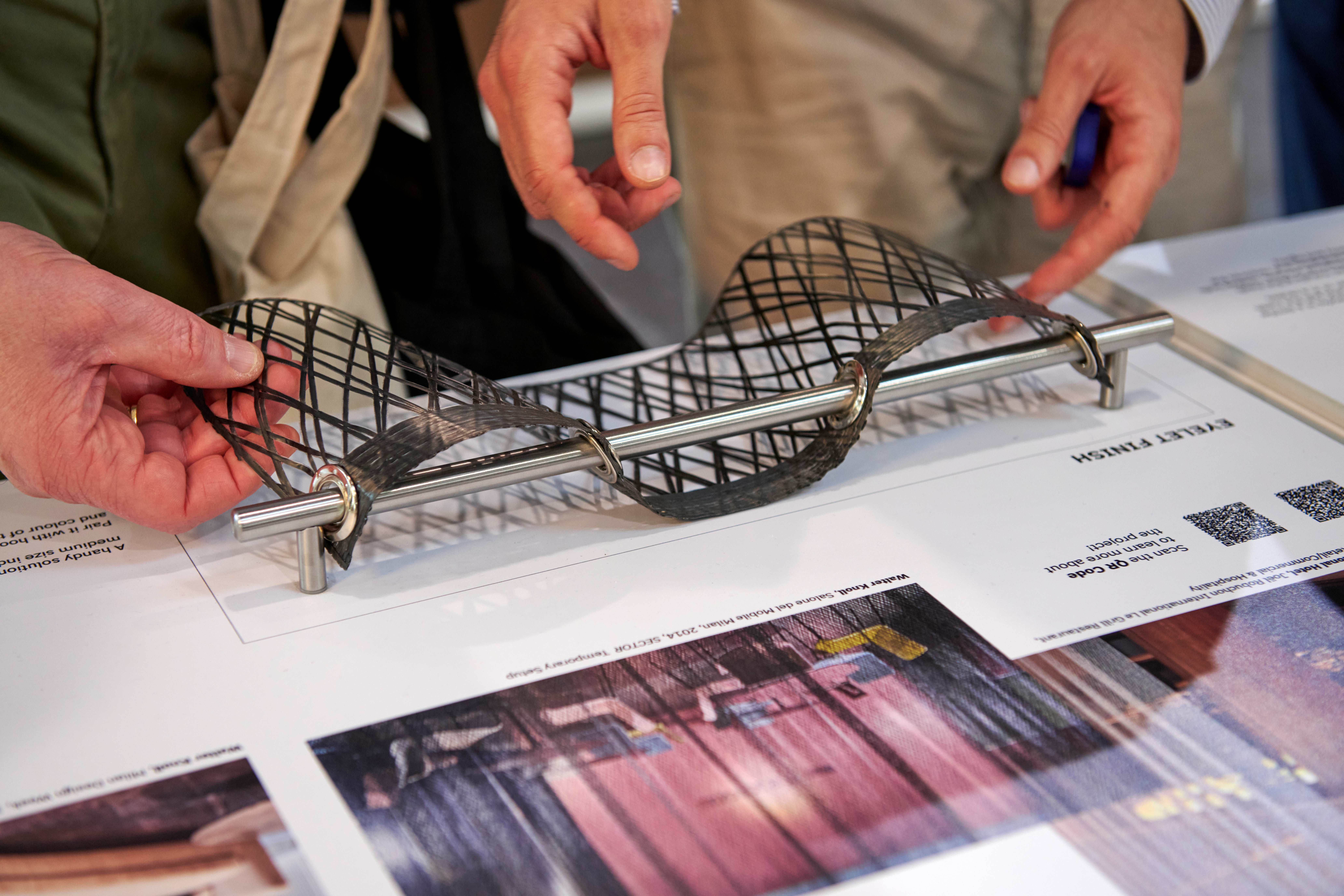 Visitor examining an i-Mesh eyelet finish mesh sample mounted on a stainless steel bar at Euroshop trade fair