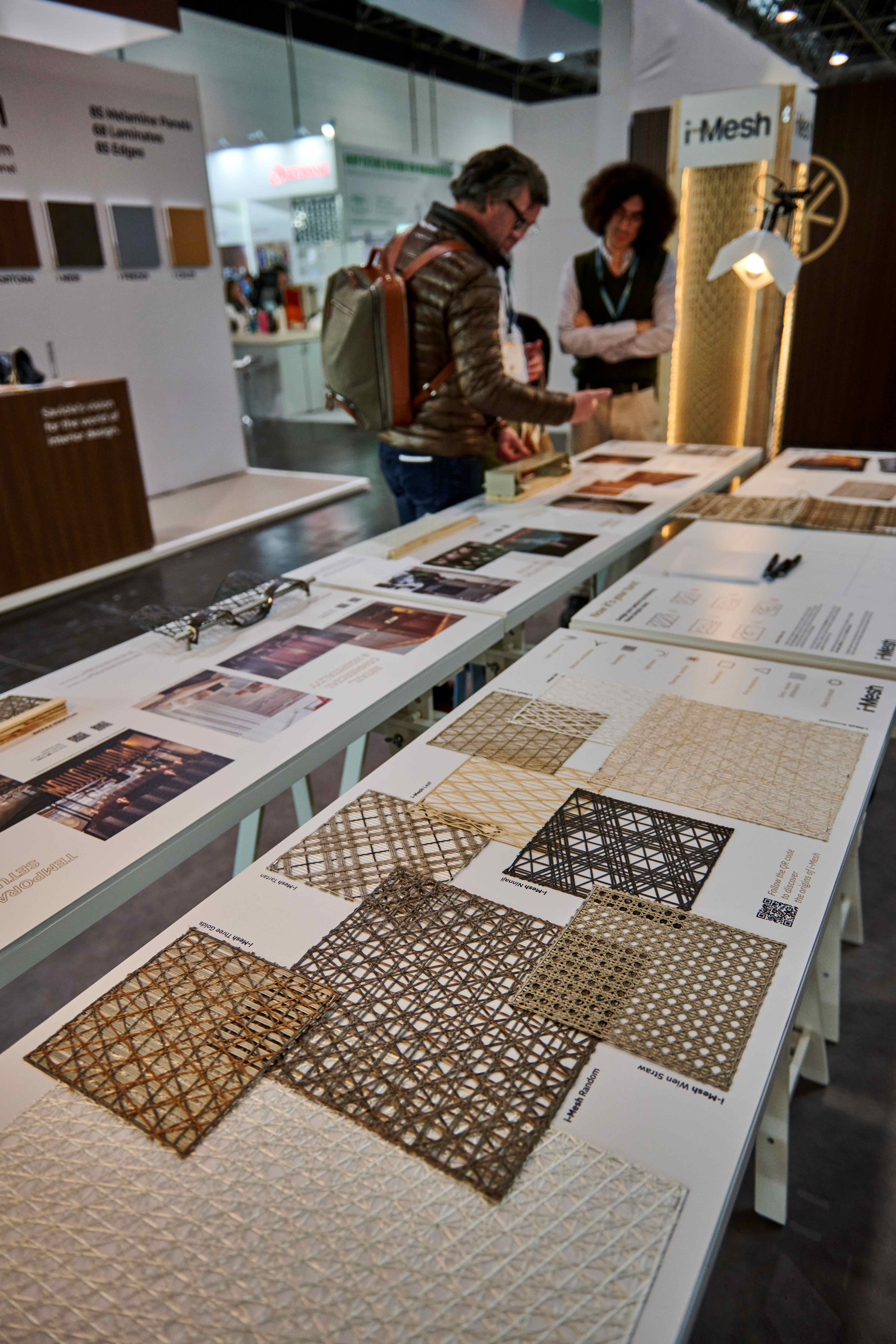 i-Mesh architectural mesh material samples displayed on stand table at Euroshop 2026, with visitors consulting the collection