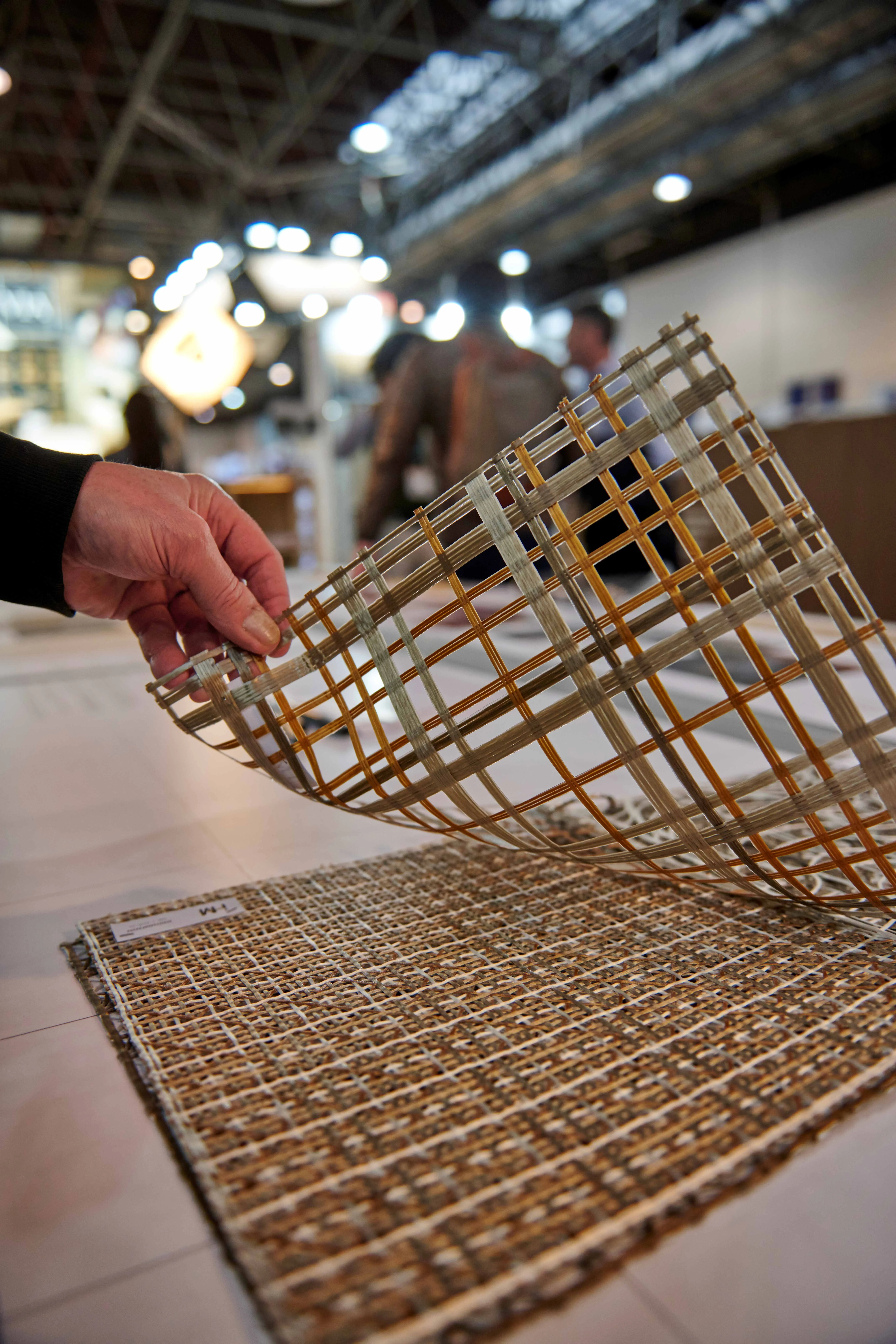Hand bending a flexible i-Mesh woven mesh sample to show material flexibility at Euroshop 2026