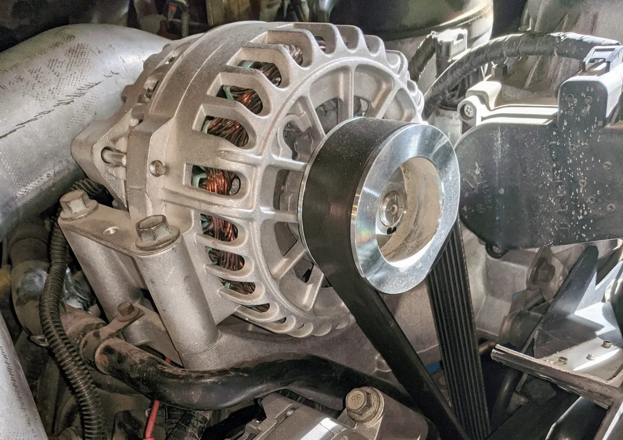 Heavy-duty alternator installed with serpentine belt, showing copper windings and mounting brackets.