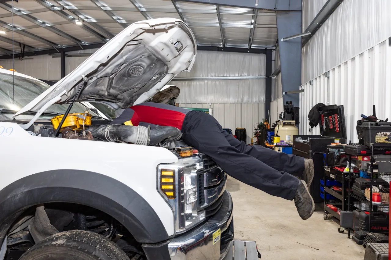 Truck engine repair on a white Ford with hood open; technician leans into engine bay, and tool cart reads AUTEL.