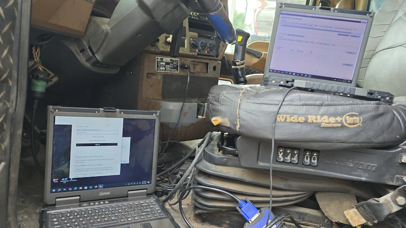 Diagnostic with rugged laptops connected inside a heavy-duty truck cab for electronic troubleshooting.