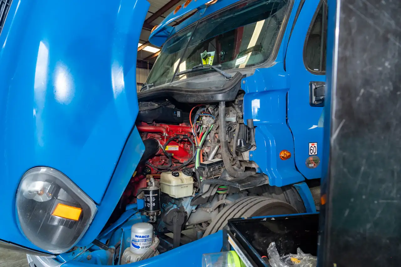 Heavy-duty repair on a blue semi-truck with the hood open, exposing the engine for maintenance. WABCO and Cummins filters are visible.