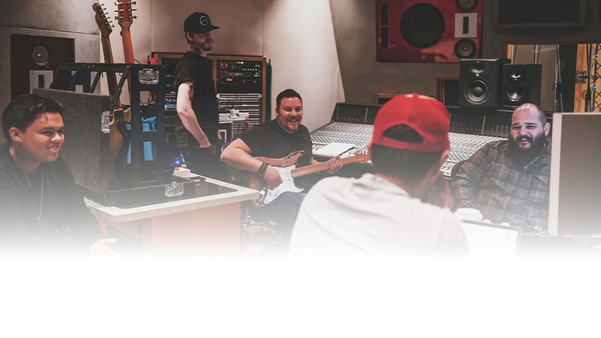A group of artists with guitars and other studio equipment gather around a mixing console in a recording studio to collaborate on music.